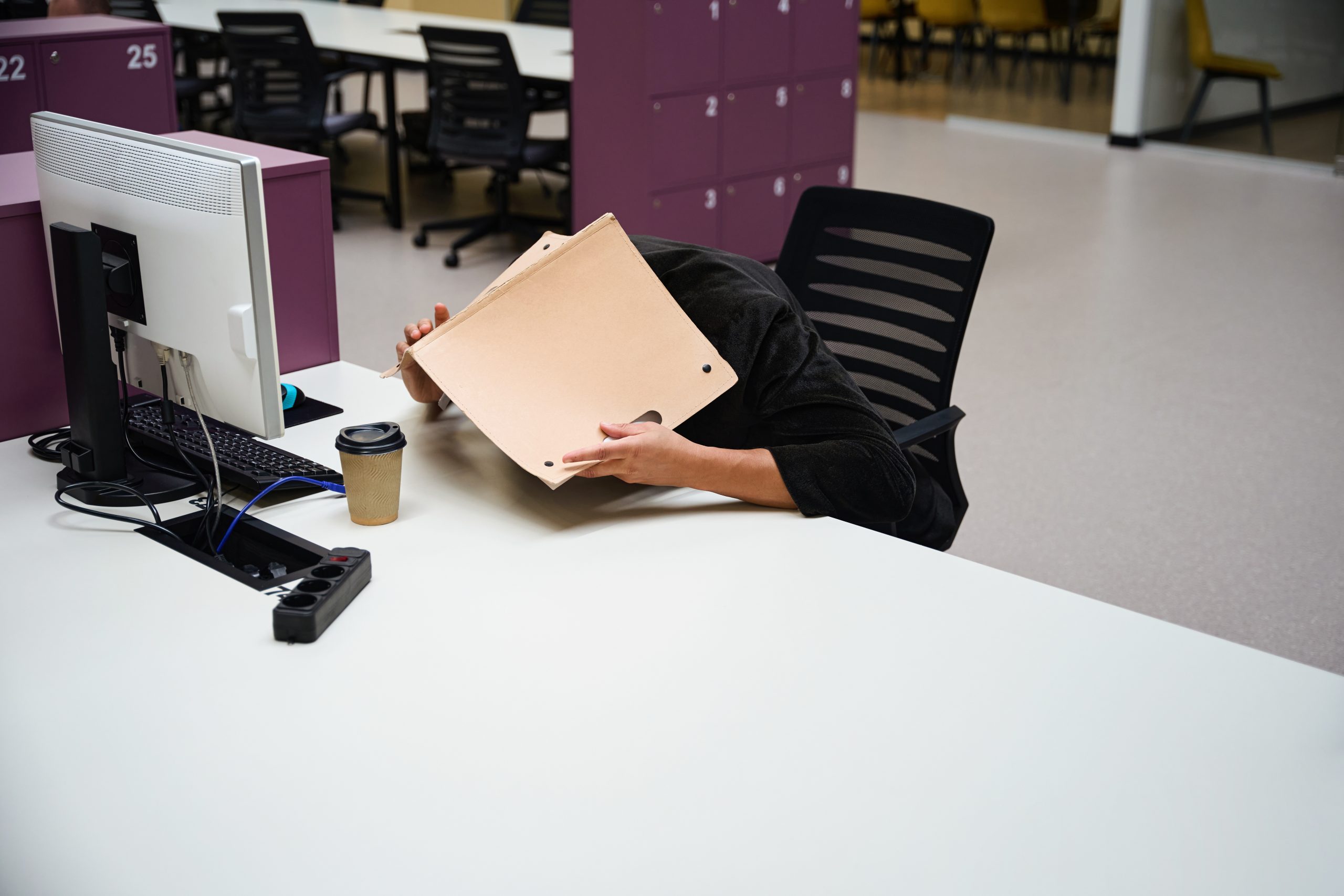 Man sitting at table while covering head with folder